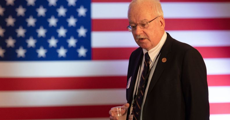 Arizona State representative John Kavanagh speaks down to a member of the crowd while holding a glass of water, an American flag behind him.