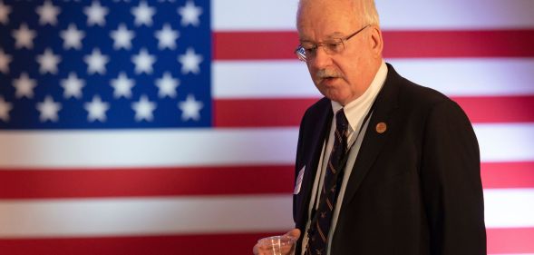 Arizona State representative John Kavanagh speaks down to a member of the crowd while holding a glass of water, an American flag behind him.
