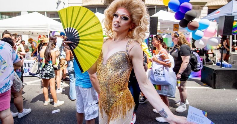 A drag queen uses a yellow hand fan during a crowded Pride event