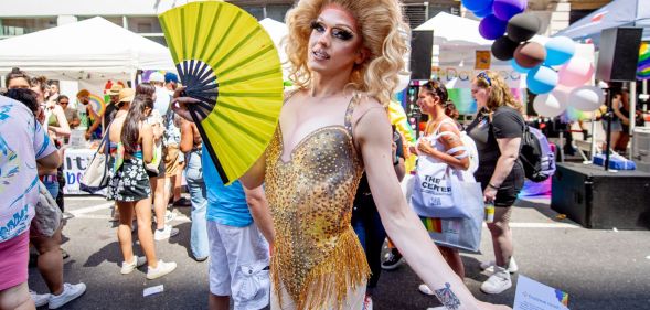 A drag queen uses a yellow hand fan during a crowded Pride event