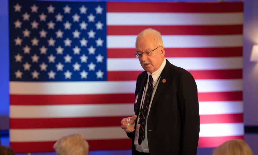 Senator John Kavanagh of Arizona, holds a cup of water while talking to a member of the crowd in frornt of an American flag.
