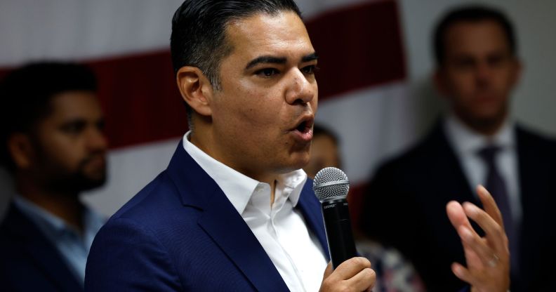 Robert Garcia, holding a microphone, speaks to a group of people in an open collar blue blazer.