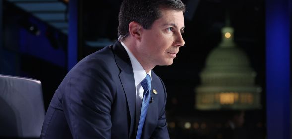 Pete Buttigieg, arched forward, sits during a Fox News broadcast while wearing a suit and blue tie.