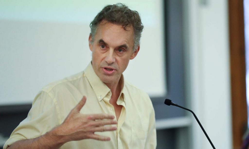 Jordan Peterson speaks during a lecture while wearing a slightly yellow t shirt