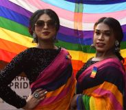 Members of the LGBTQ+ community in India stand infront of a Pride rainbow flag.