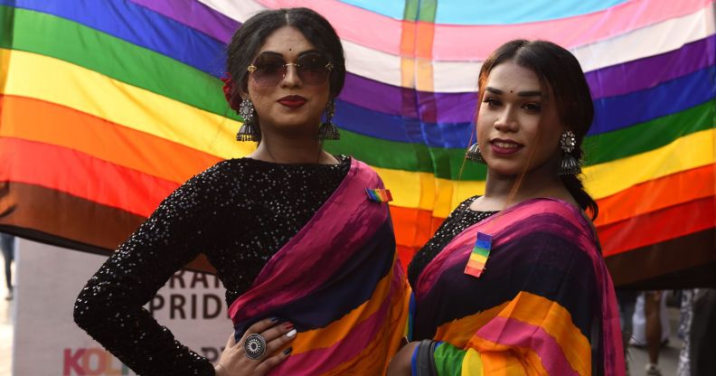 Members of the LGBTQ+ community in India stand infront of a Pride rainbow flag.