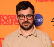 Simon Bird, wearing a cream top, smiles against an orange backdrop.