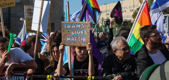 A group of individuals hold up LGBTQ+ positive signs, with one reading "trans lives matter."