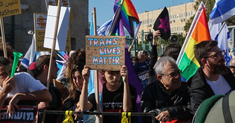 A group of individuals hold up LGBTQ+ positive signs, with one reading "trans lives matter."
