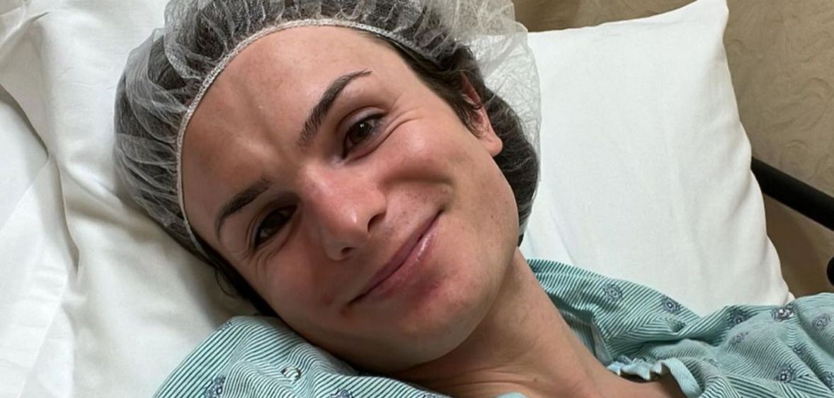 Dylan Mulvaney, head tilted, smiles while lying down in a hospital bed.