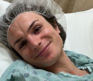 Dylan Mulvaney, head tilted, smiles while lying down in a hospital bed.