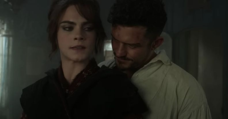 A screenshot from the new trailer of season 2 of Carnival Row shows actors Cara Delevingne and Orlando Bloom standing close together in a large room. Cara Delevingne's character Vignette Stonemoss is wearing a black dress and is looking worried and Orlando Bloom's character Rycroft "Philo" Philostrate is wearing a white shirt as he stands close behind Vignerre