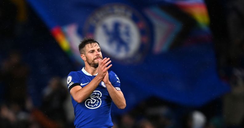 Chelsea player Cesar Azpilicueta claps during the end of a match while a Pride Chelsea flag waves in the background.