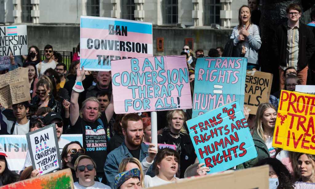 LGBTQ+ protesters holding signs that read 'ban conversion therapy', 'ban conversion therapy for all' and 'trans rights = human rights'