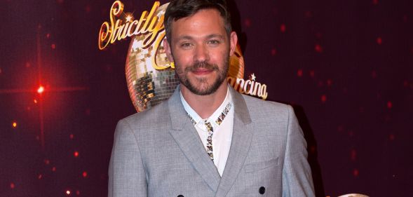 Will Young wears a great suit and white shirt as he stands in front of a red background with the Strictly Come Dancing logo