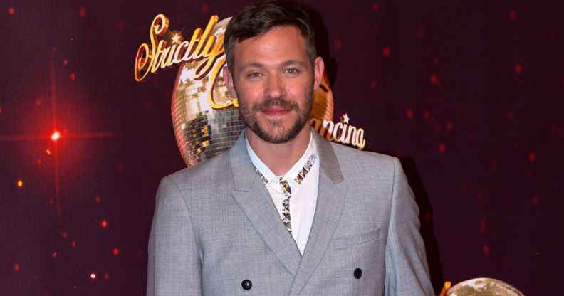Will Young wears a great suit and white shirt as he stands in front of a red background with the Strictly Come Dancing logo