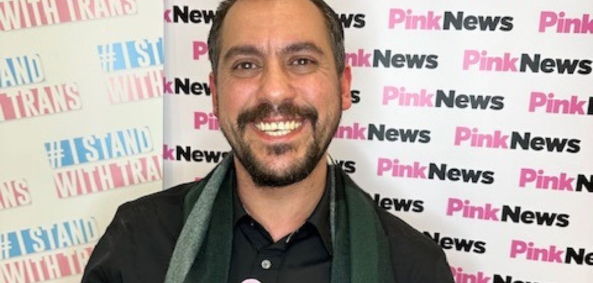 Leng Montgomery wears a dark top and green plaid scarf as he smiles at the camera after winning the Trans in the City trans corporate champion award for his work on diversity, equity and inclusion