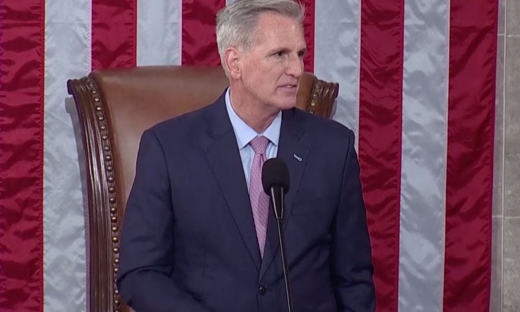 Republican congressman Kevin McCarthy, who is wearing a suit and tie, stands at a podium in front of the red, white and blue US flag as he's sworn in as speaker of the House of Representatives