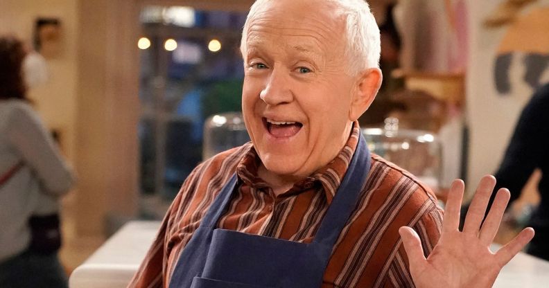 Leslie Jordan smiles and waves while wearing a red striped shirt and baking apron on the set of Call Me Kat