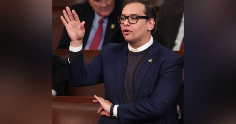 George Santos, wearing a suit, holds up his right hand to cast a vote on the US House floor while the other hand makes an 'OK' gesture