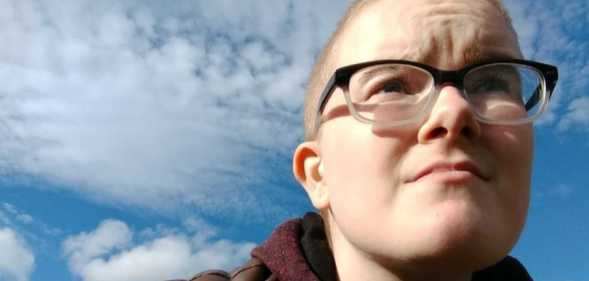 A photo shows trans man Toby Pick looking into the distance with the sky in the background