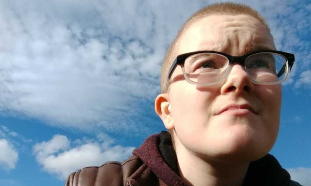 A photo shows trans man Toby Pick looking into the distance with the sky in the background