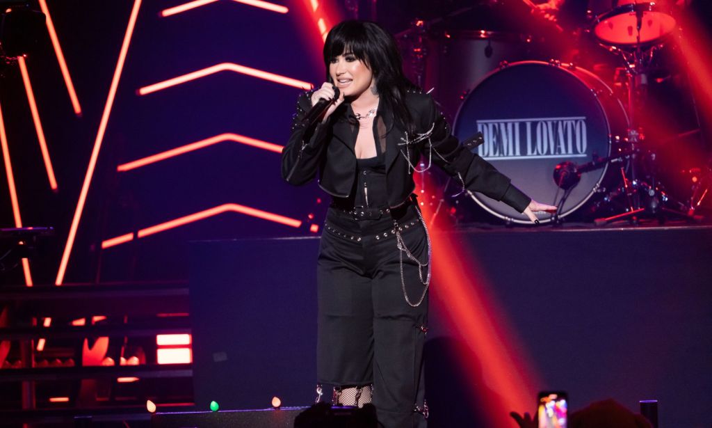 Demi Lovato sings on stage during a concert, wearing all black.