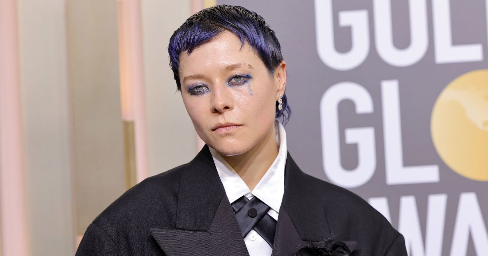 Actor Emma D'Arcy on the Golden Globes red carpet wearing a black suit with cropped purple hair.