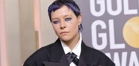 Actor Emma D'Arcy on the Golden Globes red carpet wearing a black suit with cropped purple hair.