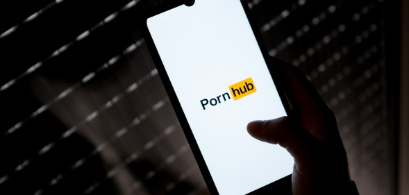 A photo shows a smartphone being held with the "PornHub" logo on a white background