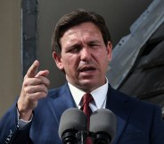 Florida governor Ron DeSantis wearing a navy suit, white shirt and red tie, stands in front of a microphone at a press conference