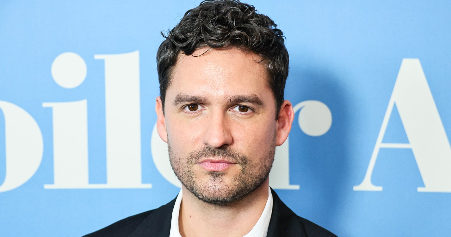 Knock at the Cabin star Ben Aldridge poses in front of a blue background
