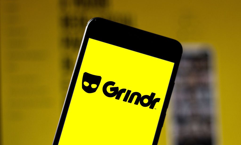 A phone showing a yellow depiction of the Grindr logo.