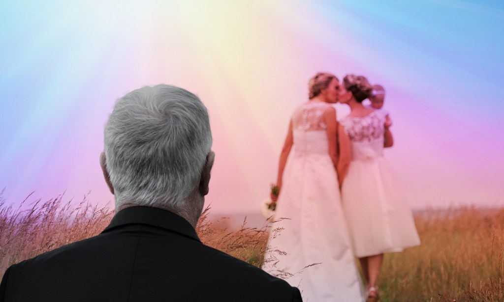 Two women kiss in wedding gowns while a man looks on