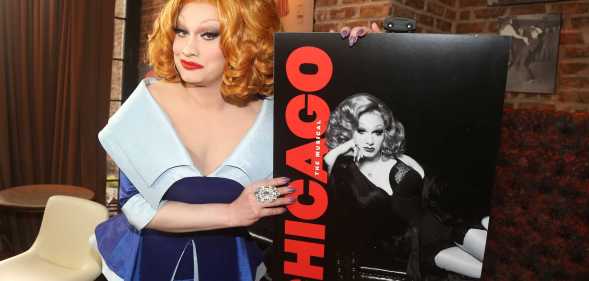 A promo photo of drag queen Jinkx Monsoon wearing a dark and light blue dress holding a poster for the Broadway production of Chicago