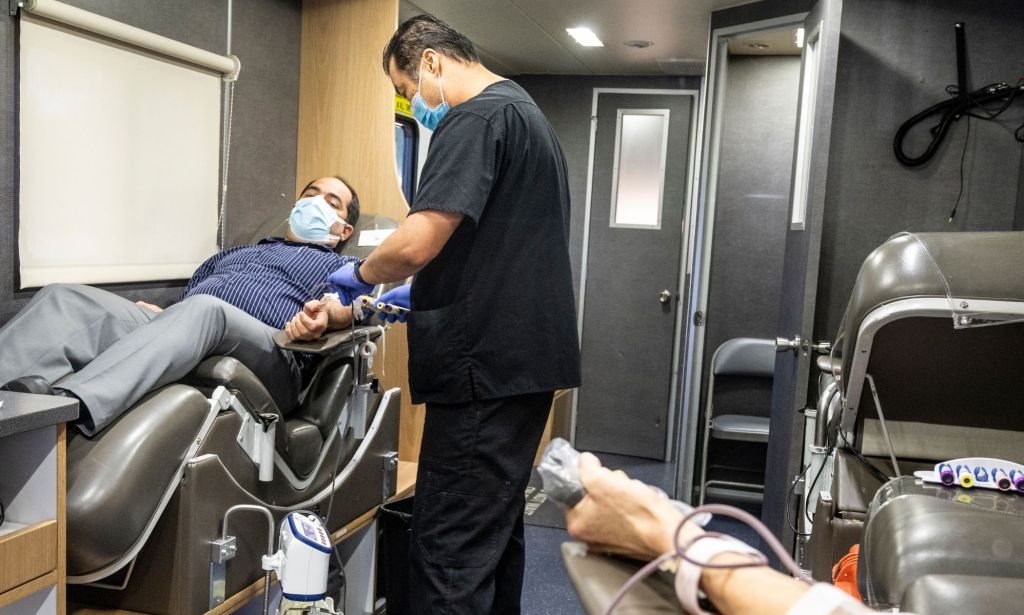 A man sits in a blood donation van as a doctor preps him for donation.