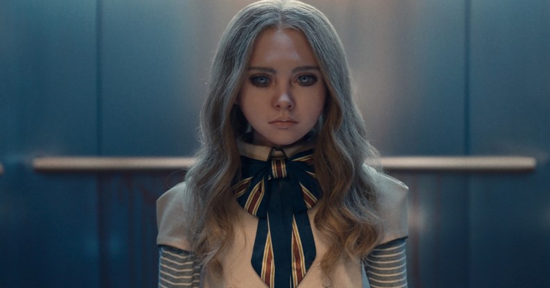 A still from the movie M3GAN showing the robot doll wearing a white and blue-striped outfit standing in an elevator