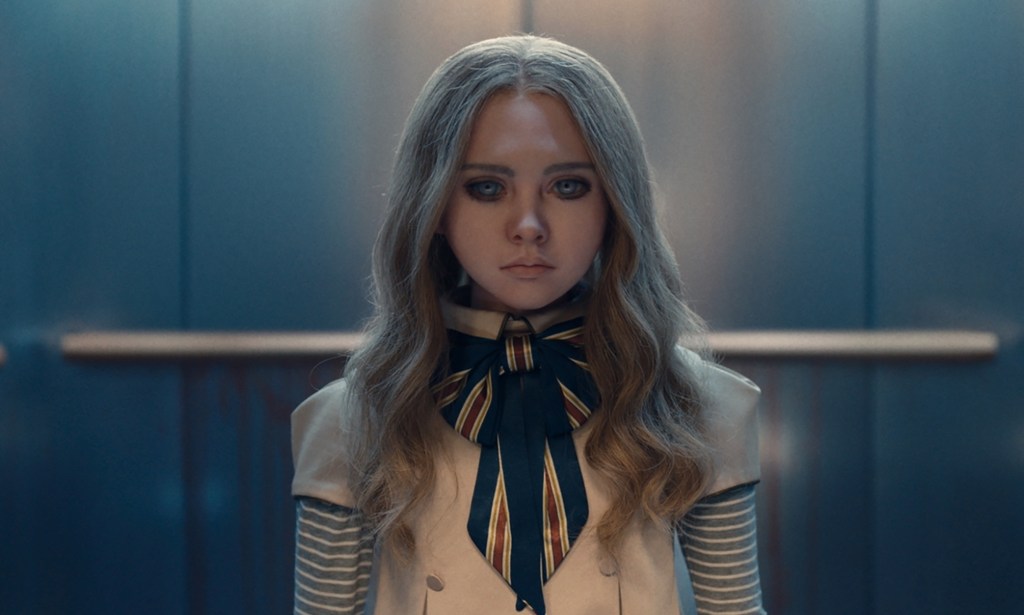 A still from the movie M3GAN showing the robot doll wearing a white and blue-striped outfit standing in an elevator