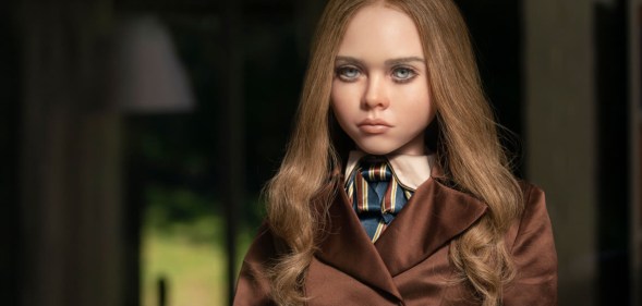 A still from the movie M3GAN shows the titular robotic doll wearing a silvery-brown coat as she stares out of a window. (Universal Pictures)