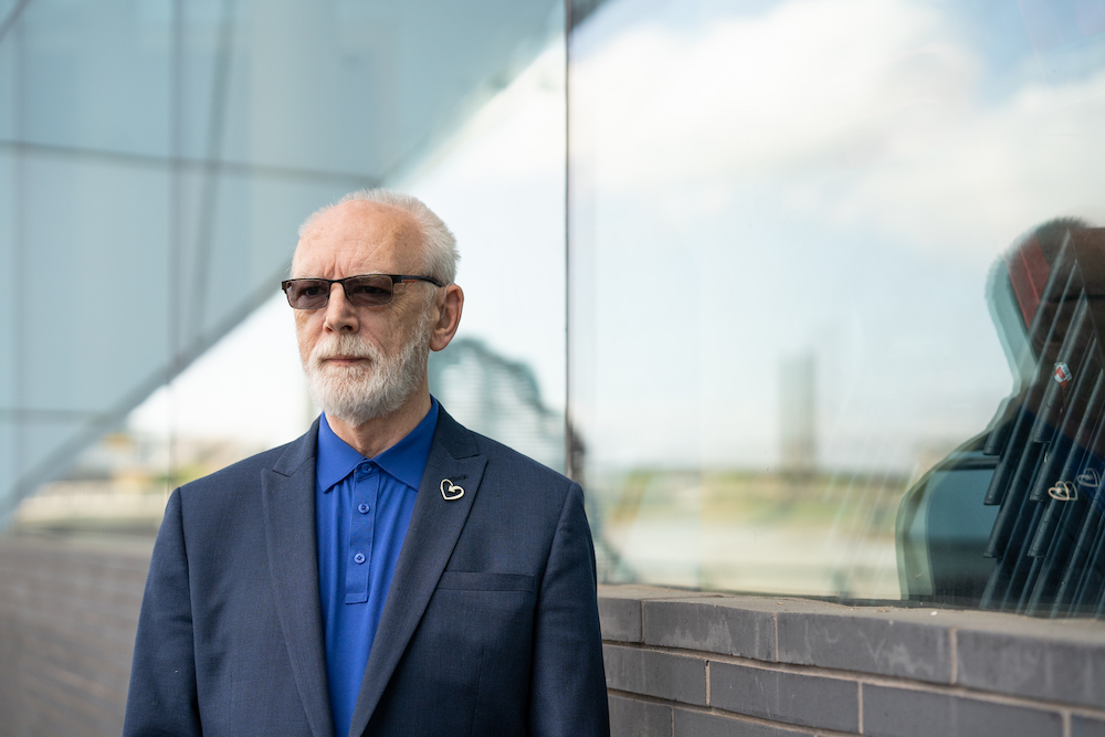 Martyn Butler, co-founder of the Terrence Higgins Trust, pictured outdoors wearing sunglasses, a grey suit and a royal blue shirt.