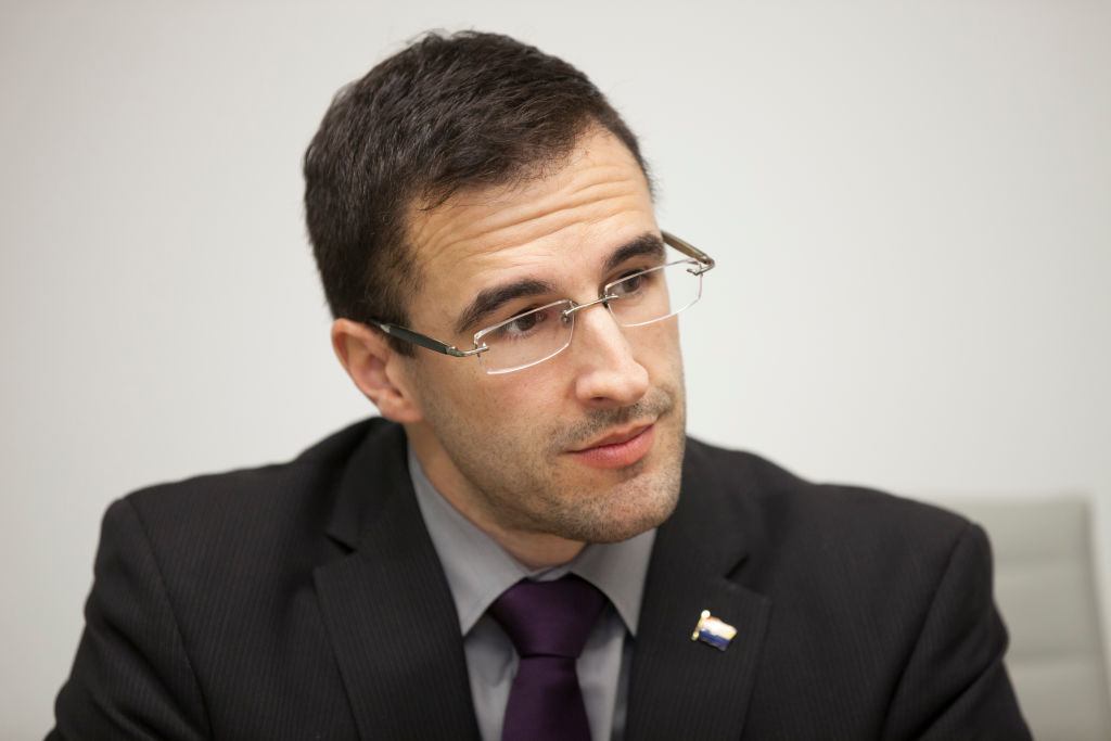 Matt Heinz during an interview in 2017. He is pictured wearing glasses and a dark suit, grey shirt and black tie against a white background.