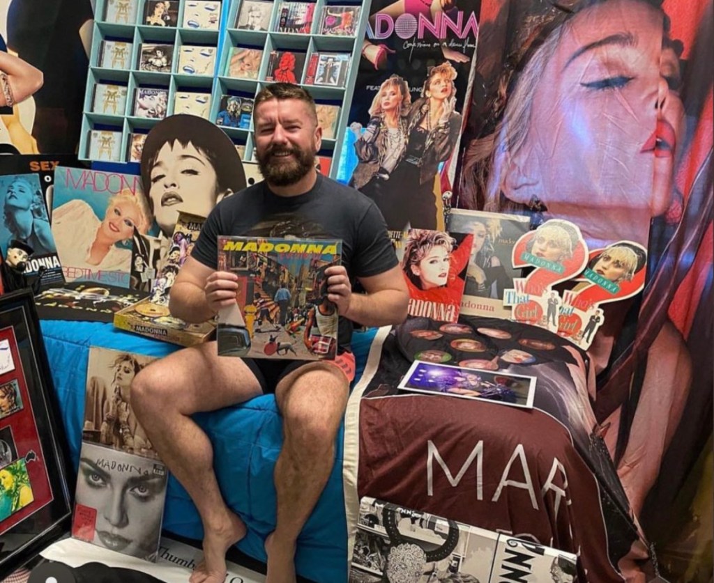 Matt, a Madonna super fan, sitting on his bed surrounded by one of the biggest Madonna merch collections in Australia