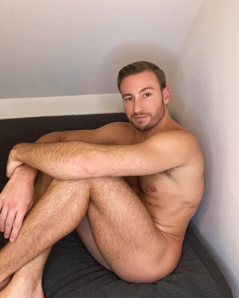 Matthew Mitcham posing nude sitting on a bed.