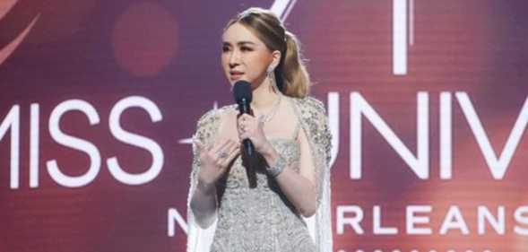 A still from the 71st Miss Universe pageant shows the franchise's owner, a trans woman called Jakkaphong "Anne" Jakrajutatip wearing a silver dress and holding a microphone standing on a stage with the "Miss Universe New Orleans" logo showing in the background