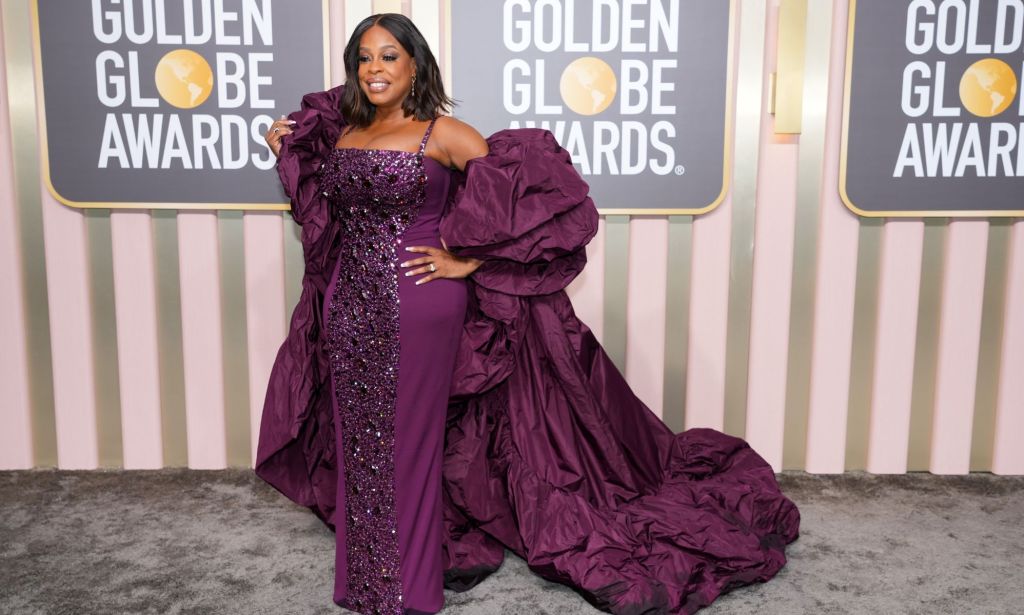 Laverne Cox in a purple gown and cape on the Golden Globes red carpet.