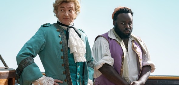 A still from HBO's Our Flag Means Death showing actors Rhys Darby and Samson Kayo dressed as pirates and standing on a ship