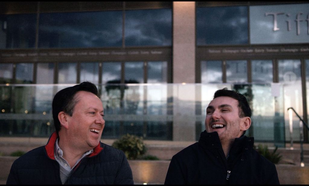 Paul (L) and Alain (R). They are sitting outdoors on a bench and both men are laughing.