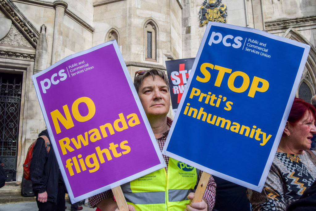 A protester holds placards opposed to the Rwanda refugee scheme during a demonstration in London. The signs read "No Rwanda flights" and "Stop Priti's Inhumanity".
