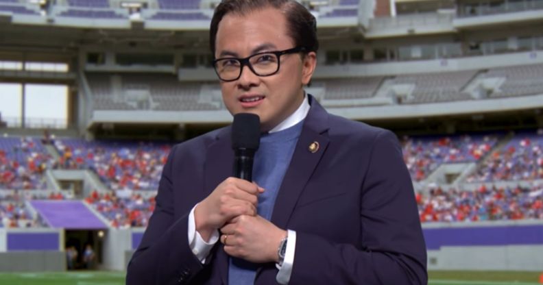 Bowen Yang dressed as George Santos during an SNL skit infront of a greenscreen of an NFL football field.