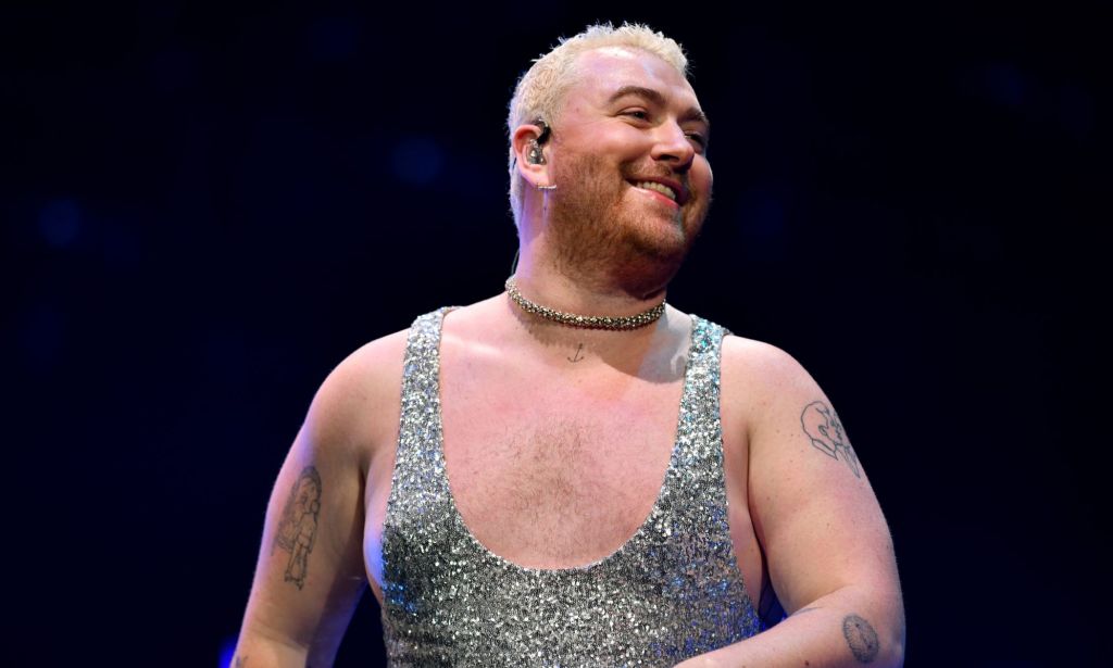 Sam Smith smiling while performing at the 2022 Jingle Bell Ball wearing a silver glittery jumpsuit